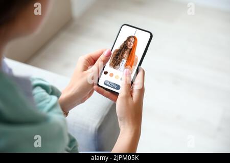 Giovane donna con un moderno telefono cellulare che utilizza l'applicazione per capelli a casa Foto Stock