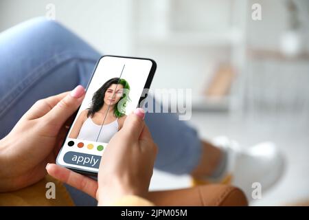 Giovane donna con smartphone che utilizza l'applicazione per capelli a casa Foto Stock