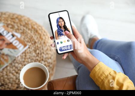 Giovane donna con telefono cellulare che utilizza l'applicazione capelli a casa Foto Stock