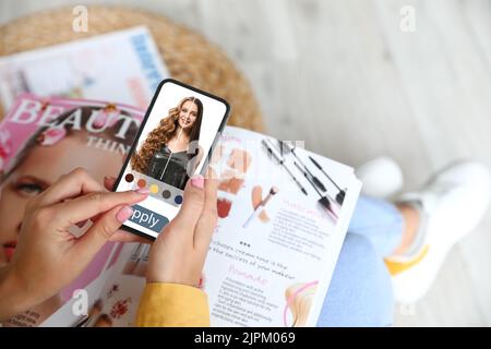 Giovane donna con telefono cellulare che utilizza l'applicazione per capelli a casa Foto Stock