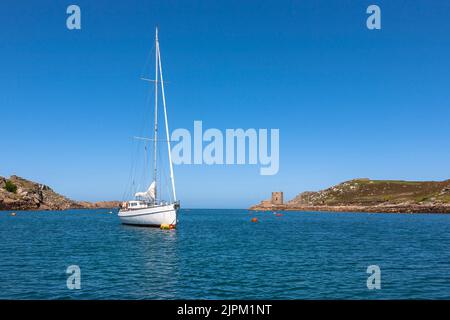 Uno yacht ormeggiato a New Grimsby Sound tra Tresco e Bryher, isole di Scilly, Regno Unito, in una tranquilla giornata estiva. Cromwell's Castle Beyond. Foto Stock