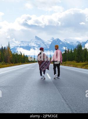 Icefields Parkway con alberi autunnali e montagne innevate nebbie a Jasper Canada Alberta. Coppia uomini e donne che camminano su strada asfaltata a Icefield parkway Foto Stock