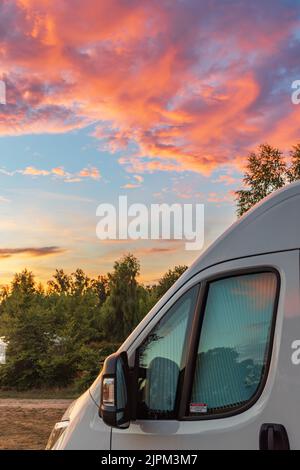 Nuvole colorate e cielo durante il tramonto con camper davanti e colori rosso arancio e blu Foto Stock