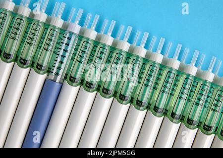 Penne per insulina diabetica allineate su uno sfondo blu. Una siringa blu in una serie di siringhe grigie. Vista dall'alto con spazio di copia Foto Stock