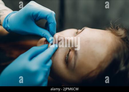 Giovane donna che fa piercing naso anello al salone di bellezza studio Foto Stock