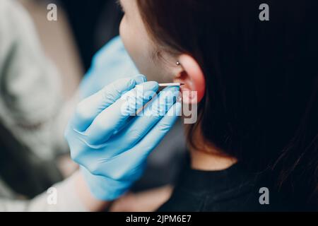 Giovane donna che fa il piercing dell'orecchio al salone dello studio di bellezza Foto Stock