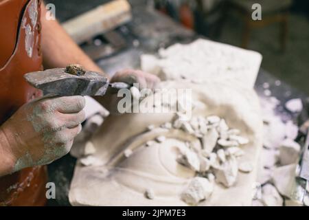 Uomo scultore crea scultura busto gesso uomo donna scultura con martello. Laboratorio di creazione di statue artigianali. Foto Stock