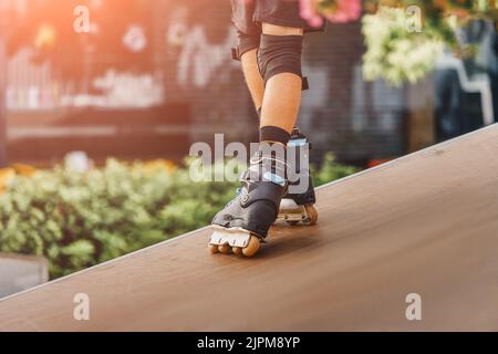 Primo piano delle gambe di uno skater a rotelle che esegue trucchi e semplicemente cavalcando sulla rampa nel parco sportivo urbano. Concetto di hobby teenage Foto Stock