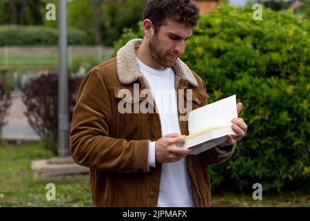 ragazzo in giacca marrone, leggendo un libro in piedi nel parco Foto Stock