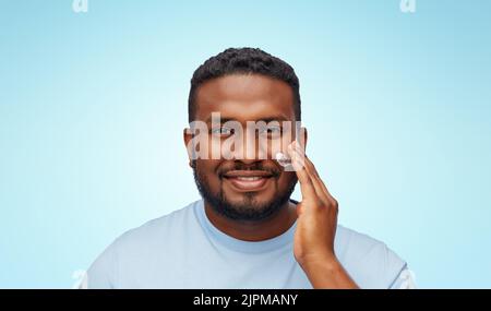 uomo afroamericano che applica idratante al viso Foto Stock