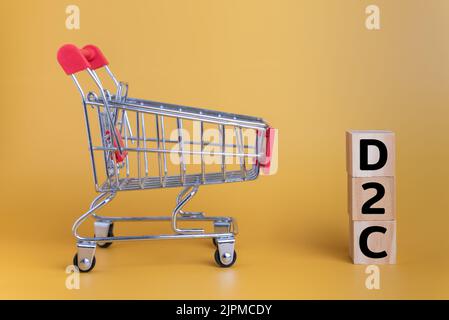 Blocco di legno testo D2C diretto al consumatore e carrello su sfondo giallo. Foto Stock