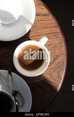 Espresso in tazze bianche su tavola rotonda in legno. Bere caffè. Foto Stock