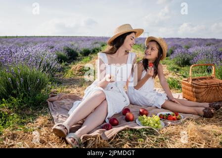 madre e bambino felici sorridendo l'un l'altro vicino alla frutta fresca su coperta in prato Foto Stock