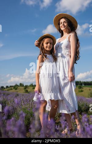 vista ad angolo basso di mamma e figlia in abiti bianchi in piedi in campo fiorente Foto Stock