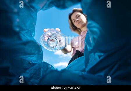 Una donna getta una bottiglia di plastica nel cestino. Primo piano dall'interno del cestino Foto Stock