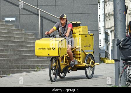 Postmistress a bordo della sua bici da carico che trasporta la posta. Posta consegna pacchi in Germania. Monaco di Baviera, GERMANIA - Agosto 2022 Foto Stock