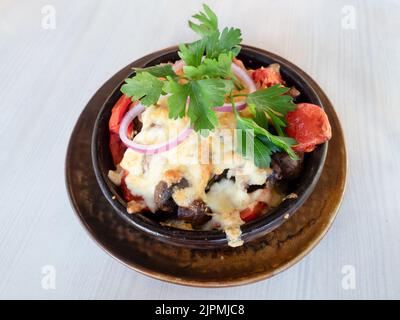 insalata caucasica di vitello, formaggio suluguni, pomodori e melanzane al forno in ciotola di ceramica su tavola di legno bianco Foto Stock