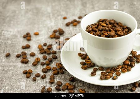 Tazza di caffè bianca con chicchi di caffè su fondo grigio in cemento con dispersione di chicchi di caffè. Arabica, robusta. Drink per l'ufficio e la casa. Backgr Foto Stock