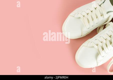 Paio di sneaker bianche su sfondo rosa. Scarpe UNISEX, sneaker bianche eleganti. Vista dall'alto, disposizione piatta, mockup con spazio di copia per il testo Foto Stock