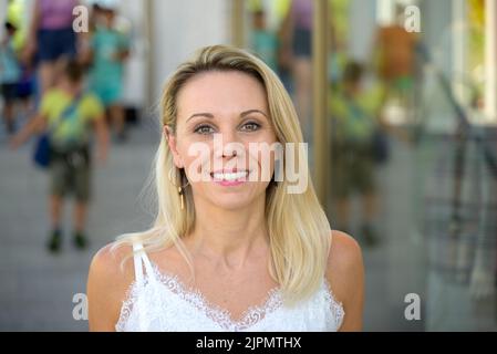 Donna bionda carina con un allegro sorriso felice in posa in una strada urbana, mentre lo shopping Foto Stock