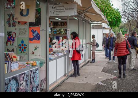 Immagine di una cliente femminile vestita in rosso che chiede un libro in uno stand della libreria alla Fiera del libro nel Parco con altre persone che camminano dietro Foto Stock