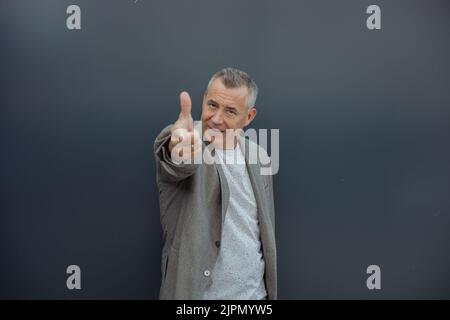 Ritratto di uomo d'affari anziano carino in piedi su sfondo grigio, puntando il dito indice verso la macchina fotografica. Stile di vita attivo. Foto Stock