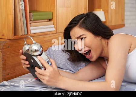 Ragazza asiatica che ha dormito troppo guardando la sua sveglia Foto Stock