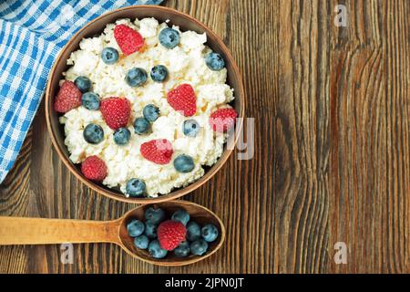ricotta con lamponi e mirtilli in una terrina di argilla marrone e cucchiaio di legno su fondo di legno marrone. Latticini, alimenti sani. Vista dall'alto Foto Stock