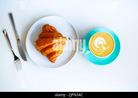 Una tazza di caffè tardivo dal design floreale sulla parte superiore e croissant sul bianco Foto Stock