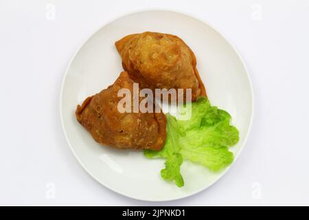 Due samosa indiane su lattuga fresca verde su piatto bianco su tela a scacchi Foto Stock