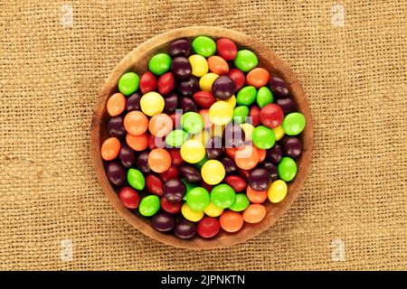 Tante caramelle dolci e colorate in una ciotola di legno sulla tela di canottaggio, primo piano, vista dall'alto. Foto Stock