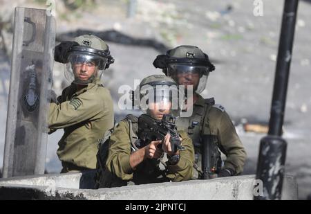 Hebron. 19th ago, 2022. Un soldato israeliano punta la sua arma contro i manifestanti palestinesi durante gli scontri a seguito di una protesta contro l'espansione degli insediamenti ebrei nella città di Hebron, in Cisgiordania, il 19 agosto 2022. Credit: Mamoun Wazwaz/Xinhua/Alamy Live News Foto Stock