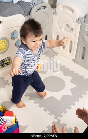 bambino di 11 mesi che cammina verso le mani aperte della madre primi passi felice Foto Stock