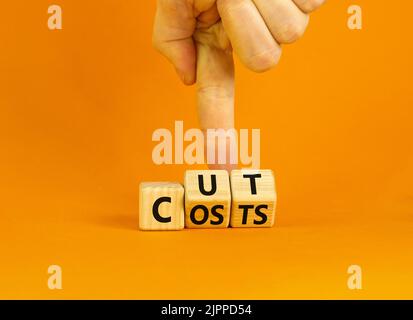 Simbolo di riduzione dei costi. Concetto parole tagliare i costi su cubi di legno. Mano dell'uomo d'affari. Bella tabella arancione sfondo arancione. Riduzione dei costi e del concetto aziendale. Foto Stock