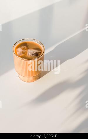 Caffè ghiacciato in vetro di cristallo sul tavolo bianco in luce naturale, ombre lunghe, foto minimalista Foto Stock