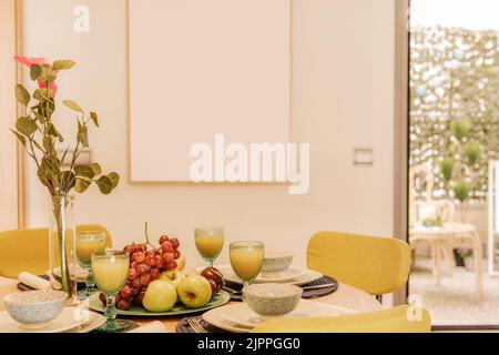 Sala da pranzo con tavolo rotondo in legno e sedie tappezzate gialle, molta frutta fresca e succo d'arancia appena spremuto Foto Stock