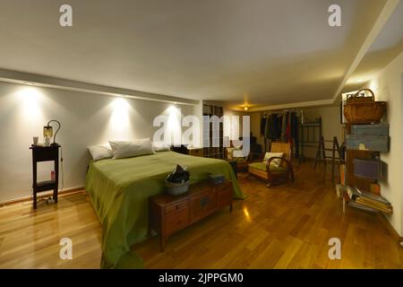 Camera da letto decorata con molti mobili e ripiani in legno, letto con copriletto verde e pavimento in parquet di quercia Foto Stock