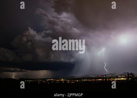 Tempesta di fulmini di notte con luci della città e cactus Saguaro Foto Stock