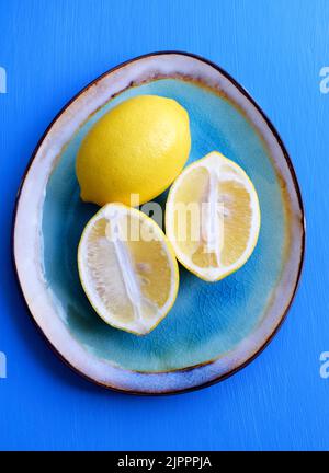 I limoni tagliati e interi su un piatto di ceramica blu con un'impazzata su uno sfondo di legno dipinto di blu. Vista dall'alto. Foto Stock