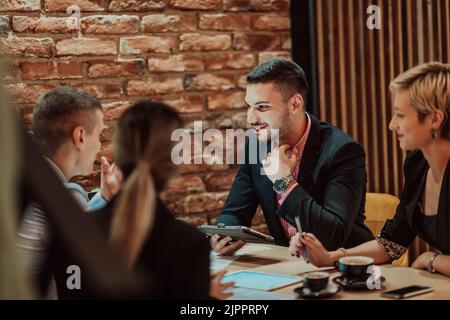 Buon uomo d'affari sorridente allegro durante una riunione in una caffetteria. Gruppo di professionisti di successo che lavorano come una squadra in un Foto Stock