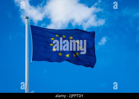 Bandiera dell'UE su sfondo blu. La bandiera dell'Unione europea sventola nel vento. Foto Stock