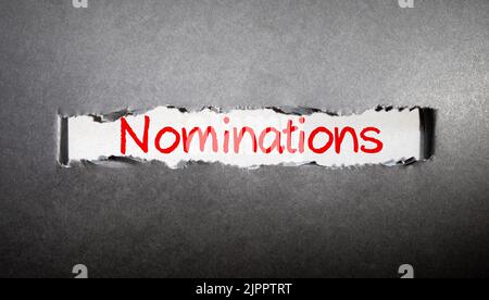 La parola NOMINE scritta su un pezzo di carta nero e un tavolo di legno Foto Stock