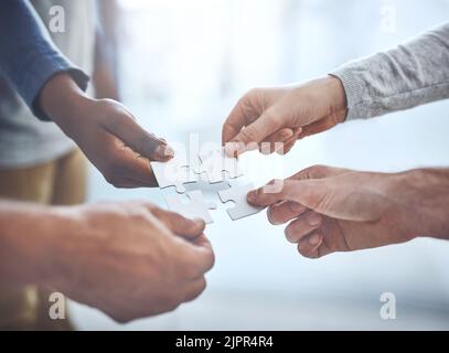 Mettere insieme la loro visione. Primo piano di un gruppo di uomini d'affari irriconoscibili che tengono insieme pezzi di puzzle. Foto Stock