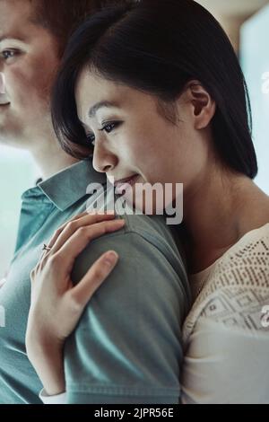 Questa è la mia spalla su cui appoggiarsi. Una giovane donna attraente che abbraccia il marito da dietro. Foto Stock