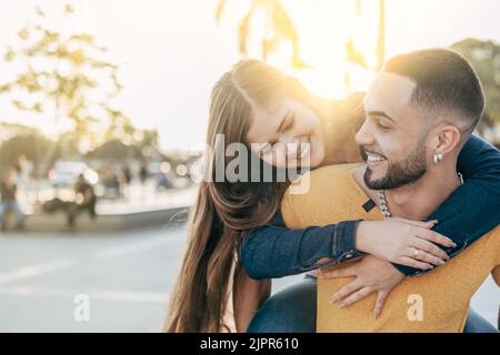 Ragazza sul piggyback del ragazzo che si diverte sulle strade della città - amici felici che ridono insieme in vacanza - concetto di gente e di vacanza - fuoco sul ma Foto Stock