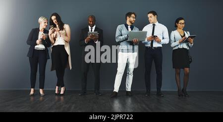 Produttività costante grazie alle connessioni wireless. Studio di un gruppo di uomini d'affari che utilizzano vari dispositivi digitali su uno sfondo grigio. Foto Stock