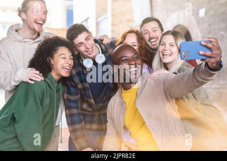 Gruppo di giovani multirazziali che prendono selfie con uno smartphone - concetto di stile di vita felice con giovani studenti che si divertono insieme - concentrarsi sull'uomo nero Foto Stock