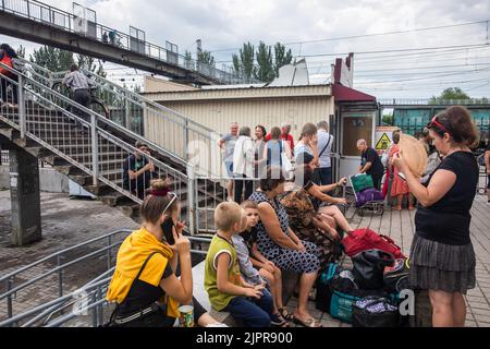 Un gruppo di persone, donne, bambini e anziani è visto seduto e in piedi sul binario, in attesa del treno. Treno di evacuazione da Pokrovsk ultima stazione ferroviaria nella regione di Donetsk. Foto Stock