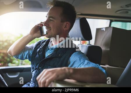 Sono in viaggio con il vostro pacchetto. Un corriere che parla su un cellulare mentre siede in un furgone di consegna. Foto Stock