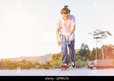 Giovani skateboarder che saltano ed eseguono un trick su una strada deserta asfaltata isolata sul cielo al tramonto - gli skater adolescenti praticano uno skateboard fuori Foto Stock